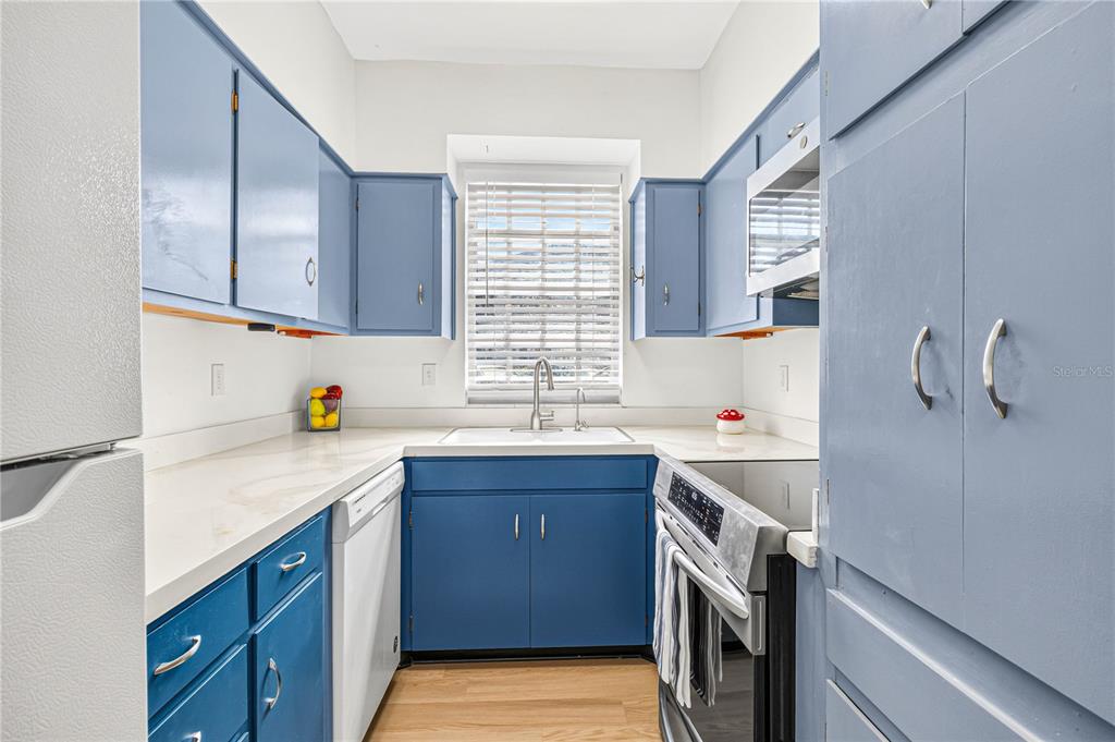 A galley kitchen features blue cabinets, white countertops, stainless steel appliances, and a window — 223 WINDSOR STREET UNIT 4, LAKELAND, FL