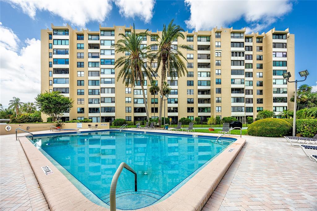 A swimming pool sits in front of a multi-story tan apartment building with palm trees — 2621 COVE CAY DRIVE UNIT 309, CLEARWATER, FL