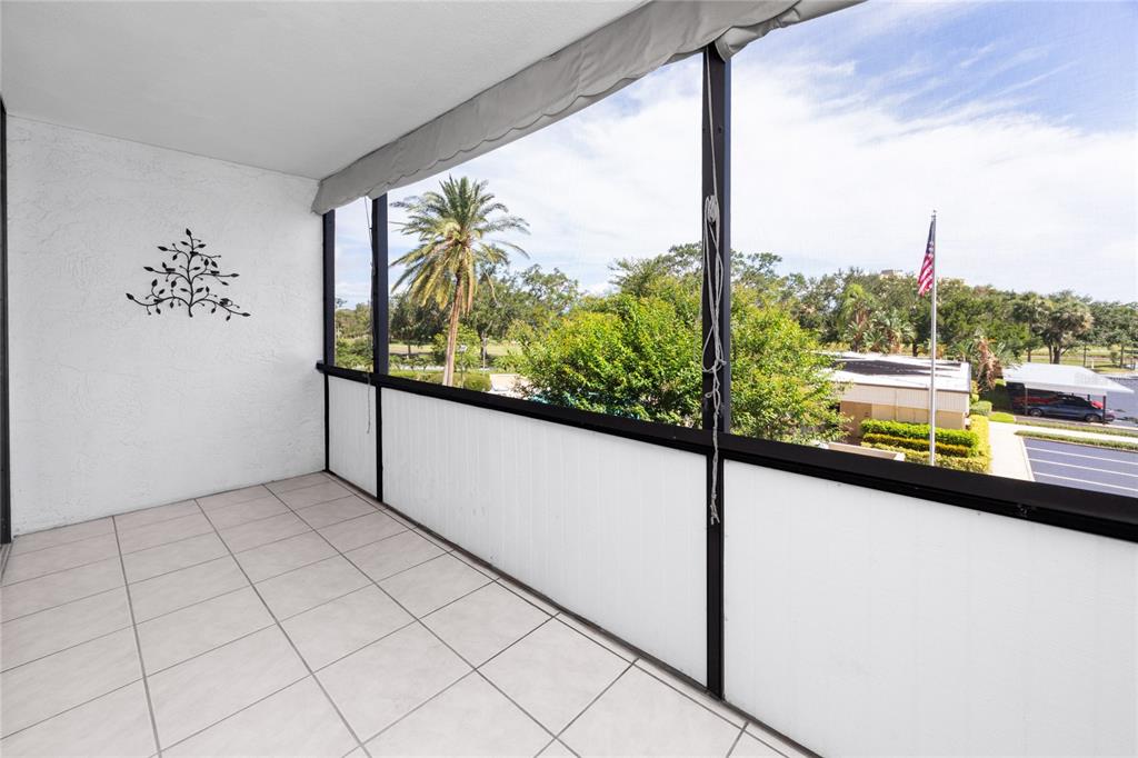 A tiled balcony features a white wall with metal decor and a screened-in view outdoors — 2621 COVE CAY DRIVE UNIT 309, CLEARWATER, FL