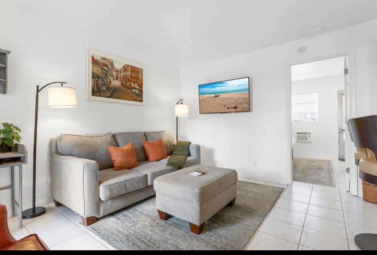 A living room features a gray sofa, matching ottoman, area rug, wall-mounted television, and floor lamps — 820 NE 16th Avenue # 3, Fort Lauderdale FL 33304, FORT LAUDERDALE, FL