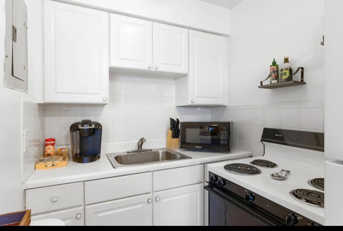 A small kitchen features white cabinets, a stainless steel sink, a microwave, and an electric stove — 820 NE 16th Avenue # 3, Fort Lauderdale FL 33304, FORT LAUDERDALE, FL