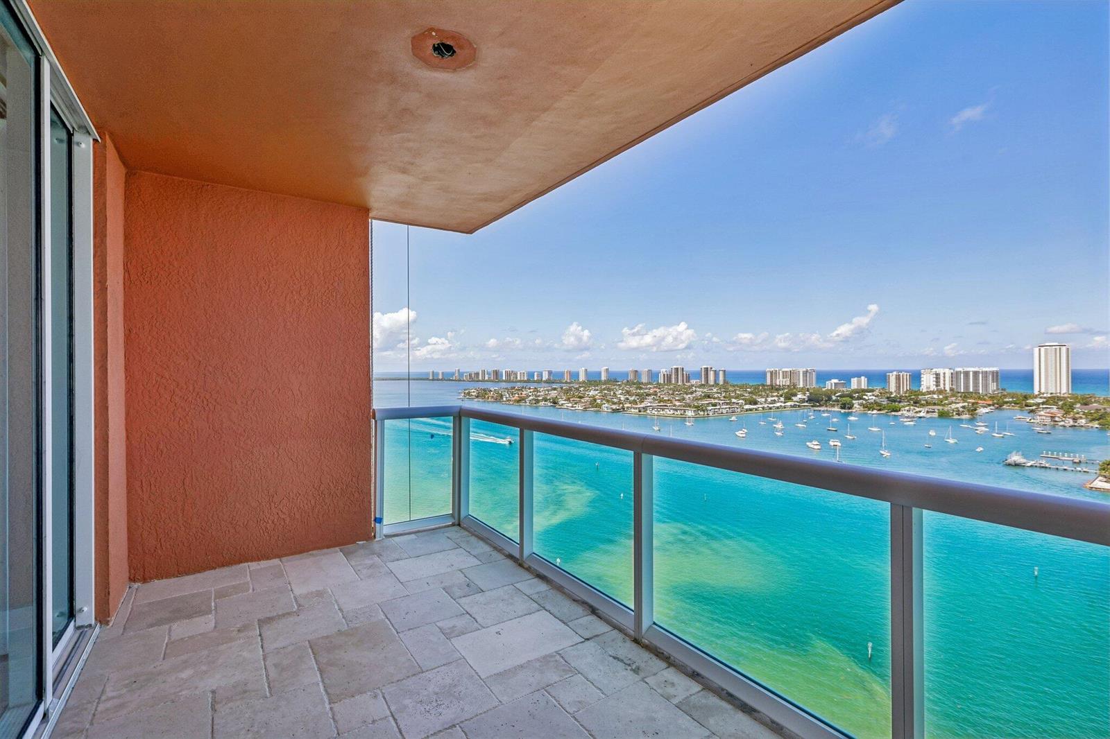 A balcony with stone tile flooring and a glass railing overlooks a turquoise bay — 2640 Lake Shore Drive # 2508, Riviera Beach FL 33404, RIVIERA BEACH, FL