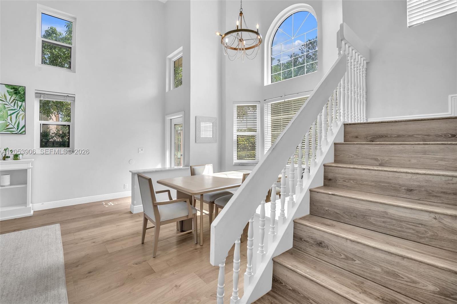 A dining area with wood floors, a white staircase, and a tall arched window — 1651 NW 104th Ave, Plantation FL 33322, PLANTATION, FL