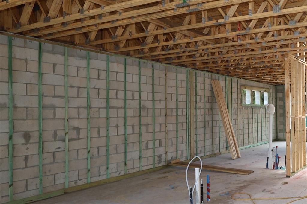 An unfinished room features concrete block walls with vertical furring strips and exposed wooden roof trusses — 17043 OVERSTORY ROAD, ORLANDO, FL