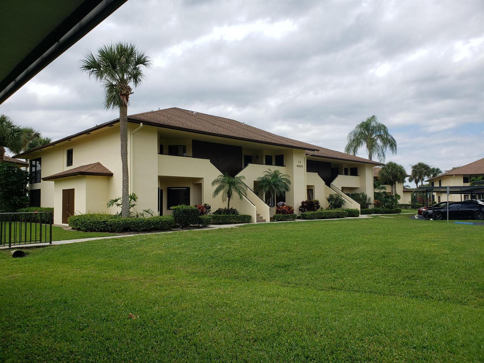 A two-story apartment building with a tan exterior, brown roof, and palm trees on grass — 6303 SE Williamsburg Drive # 201, Hobe Sound FL 33455, HOBE SOUND, FL