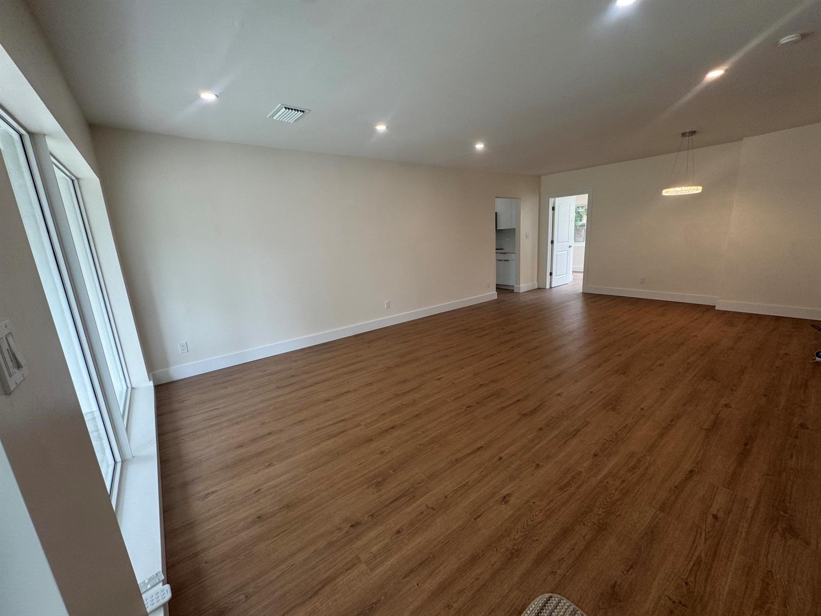 An empty room with light-colored walls, wood-look flooring, recessed lighting, and a hanging light fixture — 725 NE 160th Terrace, Miami FL 33162, MIAMI, FL