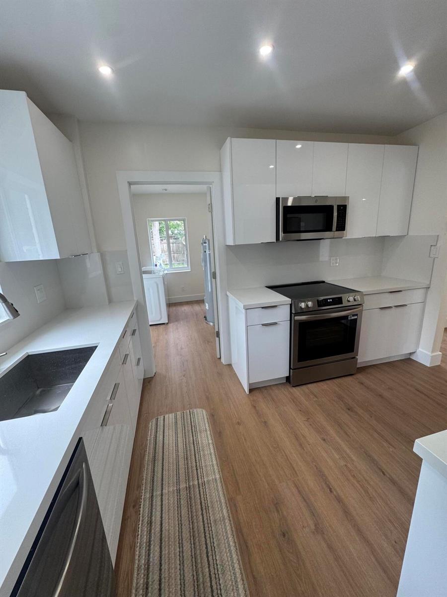 A modern kitchen features white glossy cabinets, stainless steel appliances, and light wood-look flooring — 725 NE 160th Terrace, Miami FL 33162, MIAMI, FL