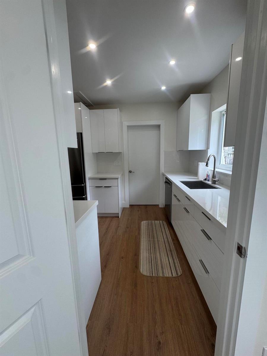 A galley kitchen features white flat-panel cabinets, quartz countertops, and wood-look flooring — 725 NE 160th Terrace, Miami FL 33162, MIAMI, FL