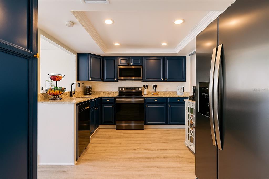 A kitchen with dark blue cabinets, stainless steel appliances, and light wood-look flooring — 4360 OUTRIGGER LANE, TAMPA, FL