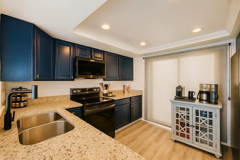 A kitchen features dark blue cabinets, granite countertops, stainless steel appliances, and light wood flooring — 4360 OUTRIGGER LANE, TAMPA, FL