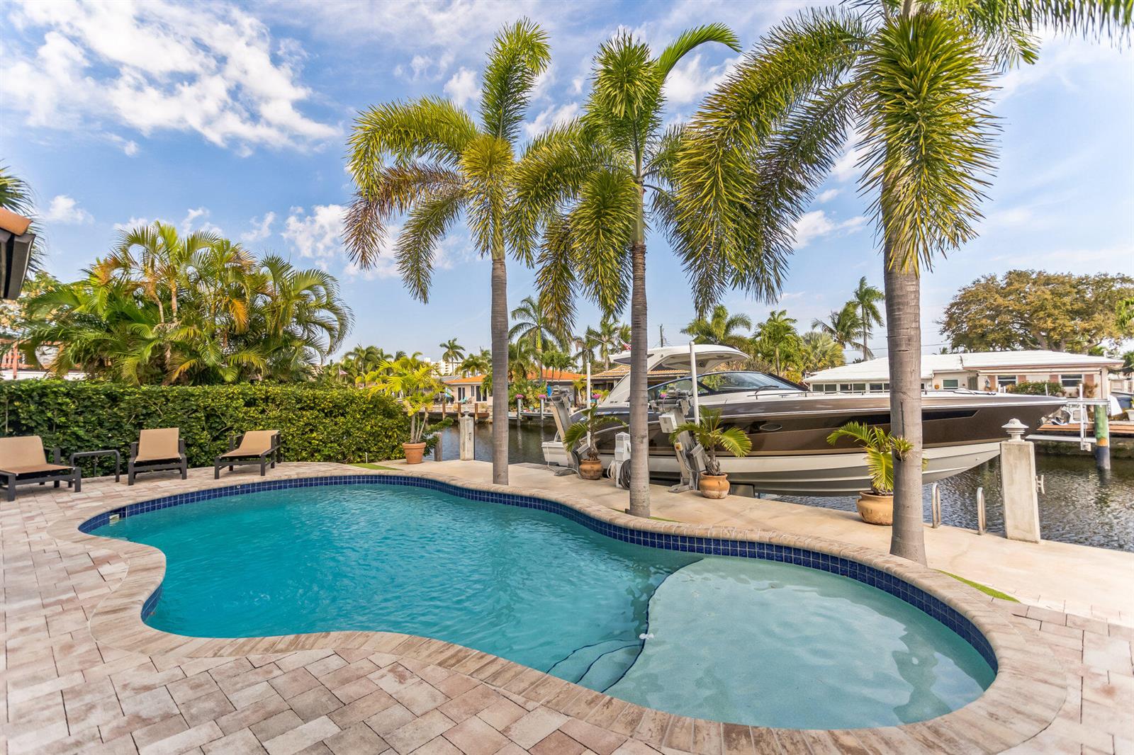A swimming pool with a tanning ledge sits on a patio next to a docked boat — 2461 SE 10th Street, Pompano Beach FL 33062, POMPANO BEACH, FL