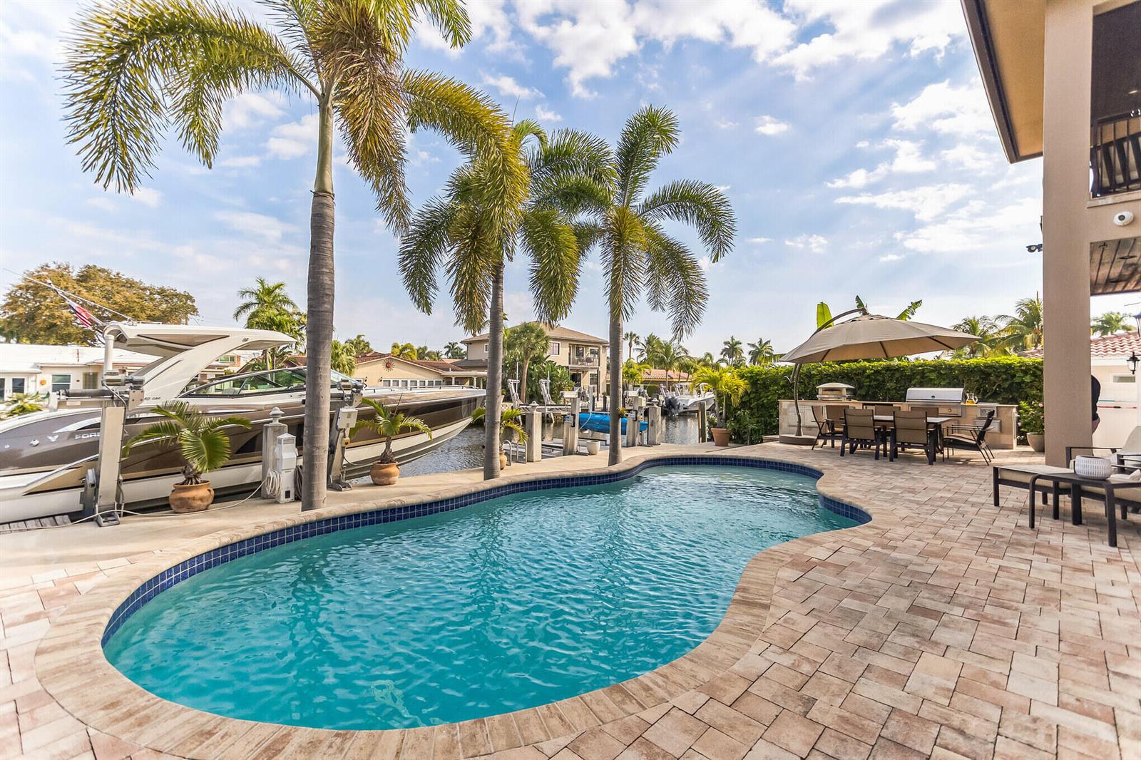 A backyard patio features a kidney-shaped pool, palm trees, a boat dock, and outdoor dining — 2461 SE 10th Street, Pompano Beach FL 33062, POMPANO BEACH, FL