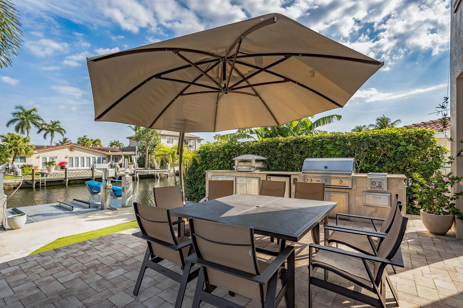 A patio with a dining set, large umbrella, and outdoor kitchen overlooking a canal — 2461 SE 10th Street, Pompano Beach FL 33062, POMPANO BEACH, FL