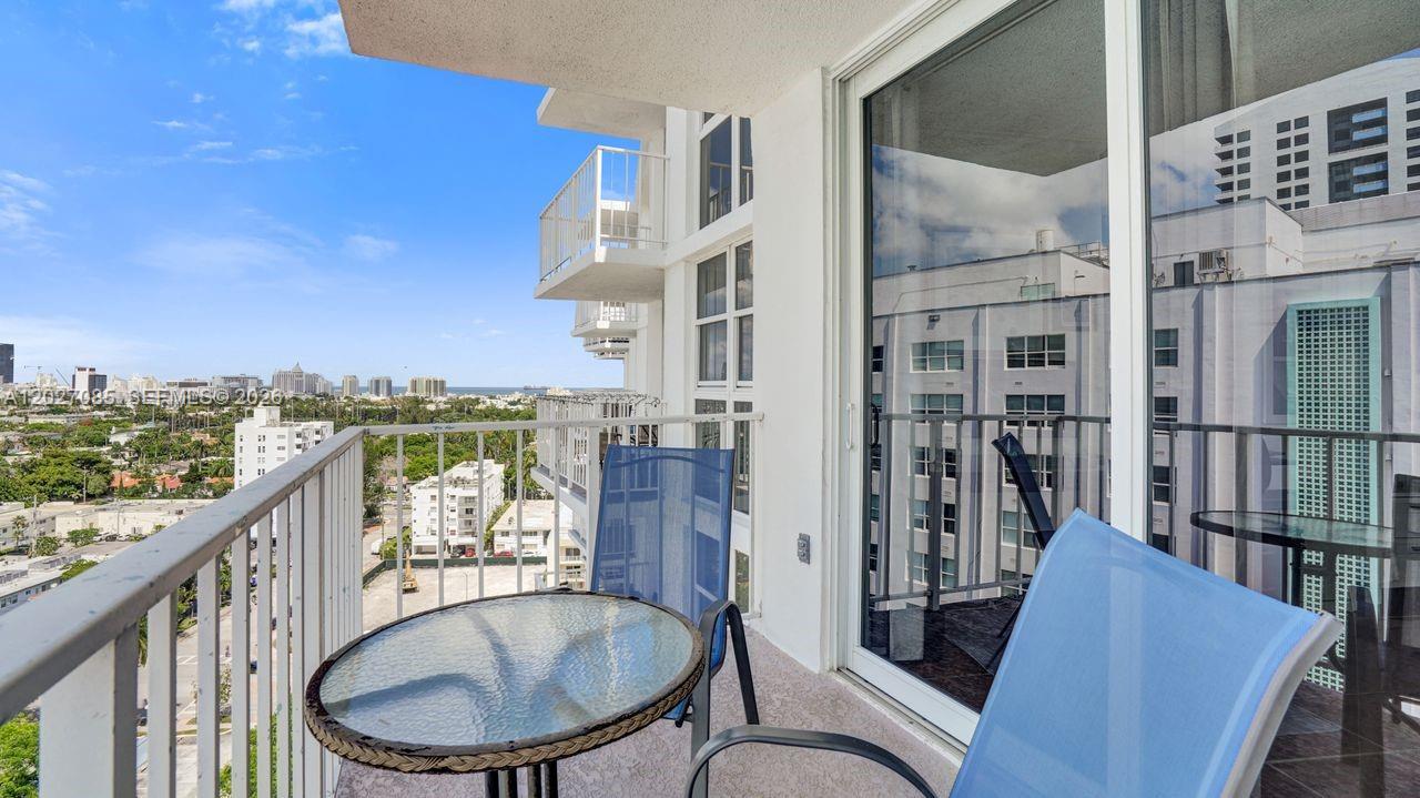 A balcony with a glass-topped table and two blue chairs overlooks a city and ocean — 1228 West Ave # 1404, Miami Beach FL 33139, MIAMI BEACH, FL