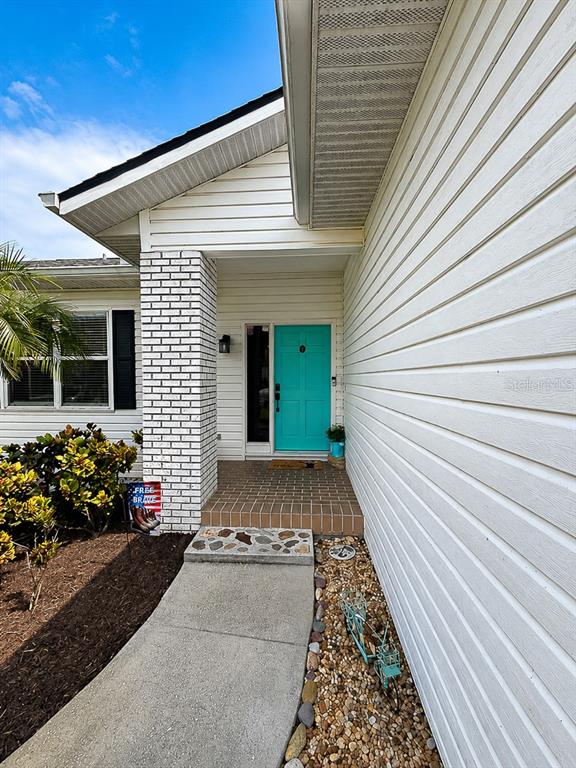 A white house exterior features a bright teal front door and a brick-accented entryway — 859 HARBOR HILL DRIVE, SAFETY HARBOR, FL