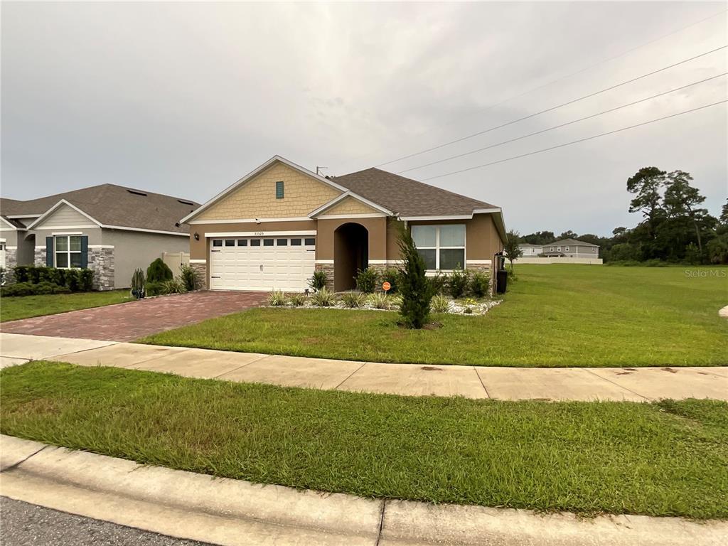 A single-story suburban house with a tan stucco exterior, stone accents, and a paved driveway — 33525 ALWAYS DREAMING COURT, SORRENTO, FL