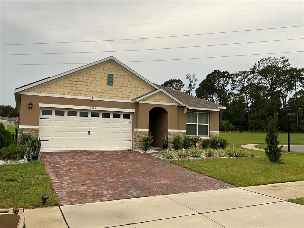 A single-story house features a brick driveway, a two-car garage, and tan siding — 33525 ALWAYS DREAMING COURT, SORRENTO, FL