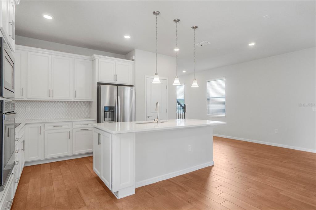 A modern kitchen features white cabinetry, stainless steel appliances, a center island, and hardwood floors — 14025 KAUAI DRIVE, ORLANDO, FL