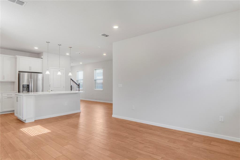 A bright, open-concept kitchen and living area features white cabinetry, a breakfast island, and wood-look flooring — 14025 KAUAI DRIVE, ORLANDO, FL