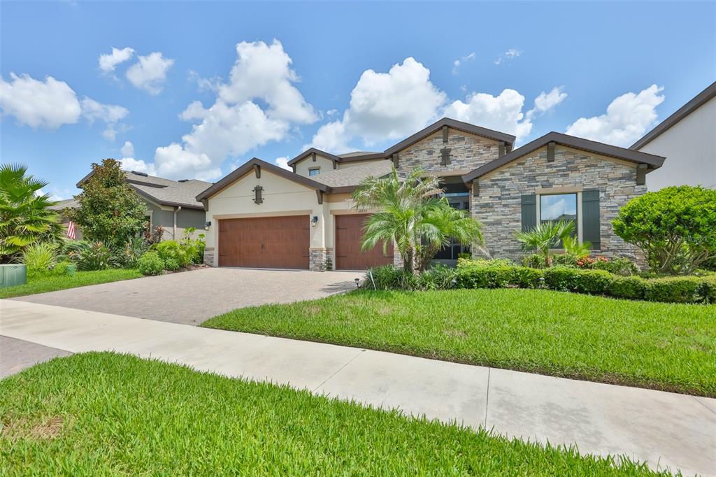 A single-story house with a stone facade, two garage doors, and a landscaped front yard — 12835 SATIN LILY DRIVE, RIVERVIEW, FL