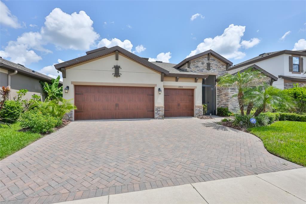 A single-story house with a three-car garage, stone accents, and a brick paver driveway — 12835 SATIN LILY DRIVE, RIVERVIEW, FL