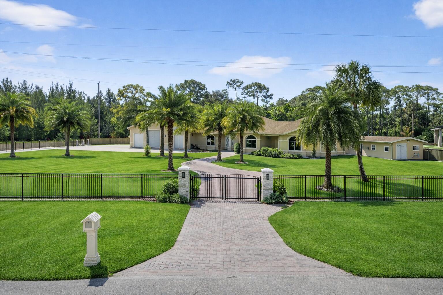 A gated driveway leads to a single-story house with a large lawn and palm trees — 12038 Key Lime Boulevard, FL 33412, FL