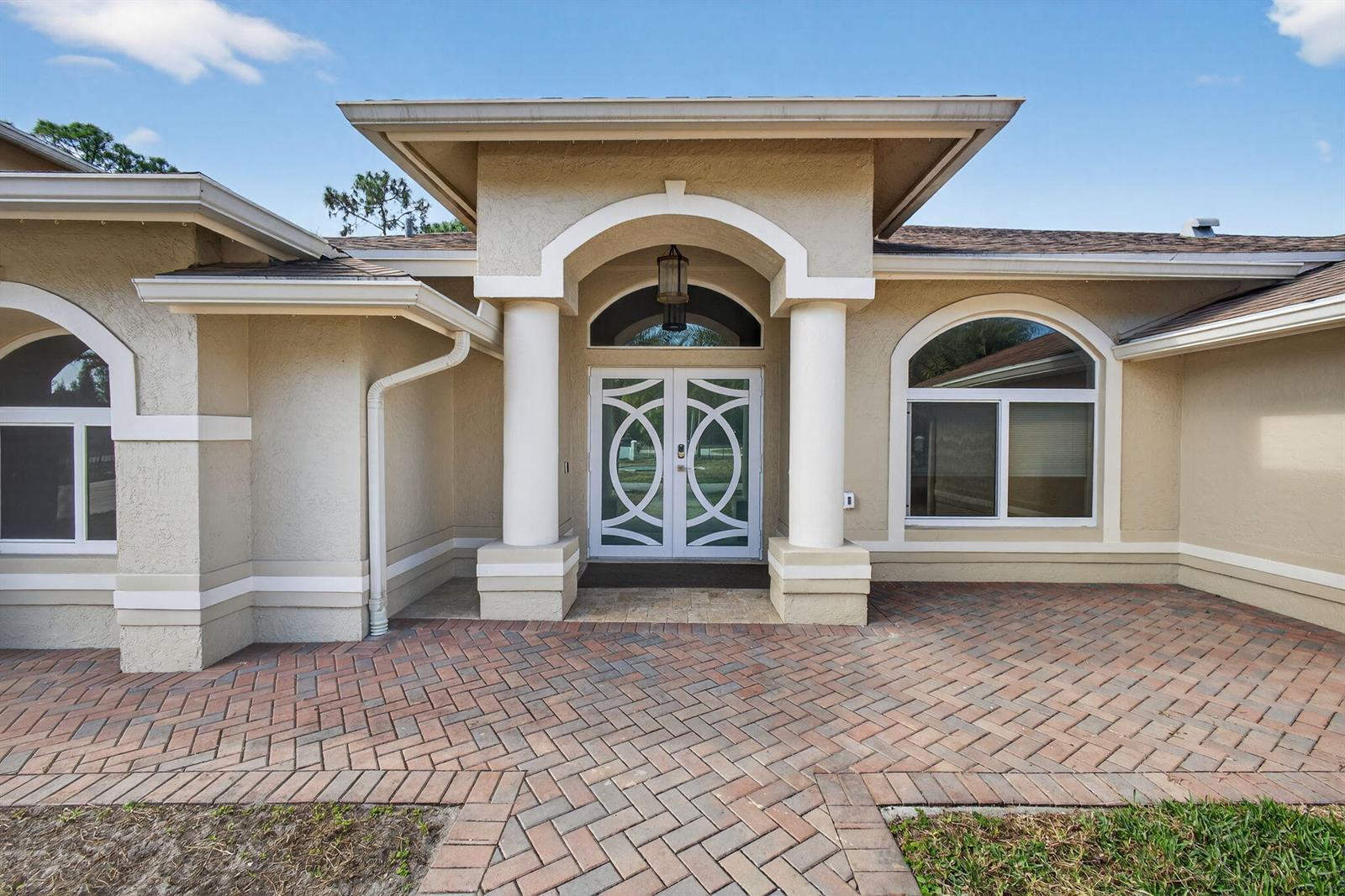 The exterior of a house features a brick paver walkway leading to a double-door entrance — 12038 Key Lime Boulevard, FL 33412, FL