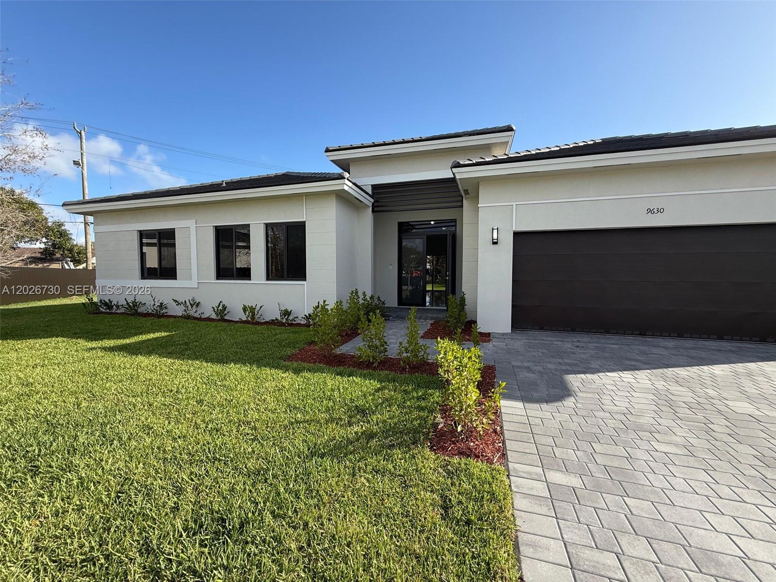 A modern single-story house features a paved driveway, a dark garage door, and landscaping — 9630 SW 208th Ter, Cutler Bay FL 33189, CUTLER BAY, FL