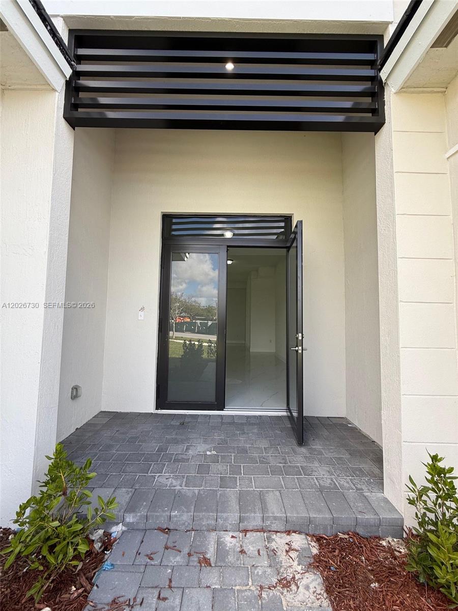 A paved entryway leads to a modern glass-paneled door with black framing and horizontal slats — 9630 SW 208th Ter, Cutler Bay FL 33189, CUTLER BAY, FL