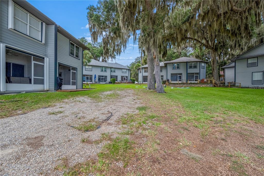 A gravel path leads toward several multi-story gray residential buildings surrounded by large mossy trees — 21116 NE 101ST AVENUE UNIT 10, EARLETON, FL