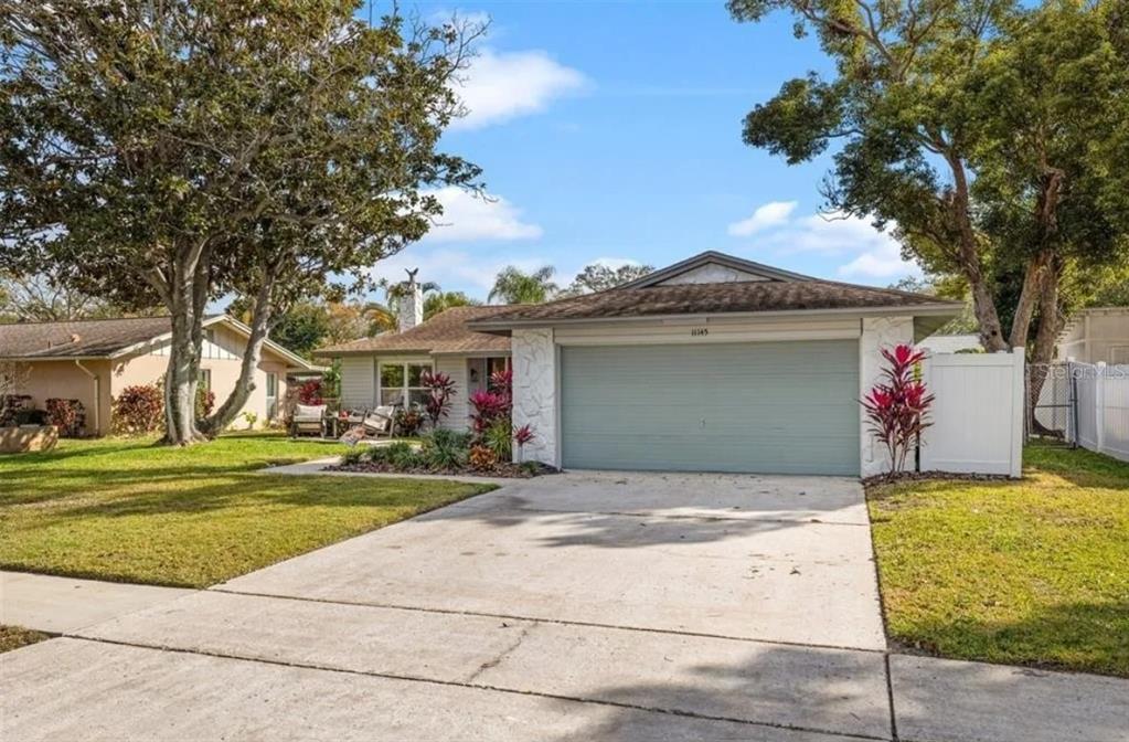 A single-story house with a light-colored exterior, a two-car garage, and a concrete driveway — 11145 BELLA LOMA DRIVE, LARGO, FL