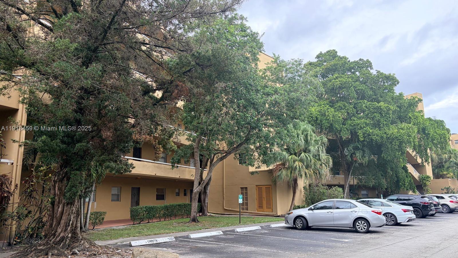 An exterior view of a multi-story tan apartment building with a parking lot in front — 4111 Stirling Rd # 102, Dania Beach FL 33314, DANIA BEACH, FL