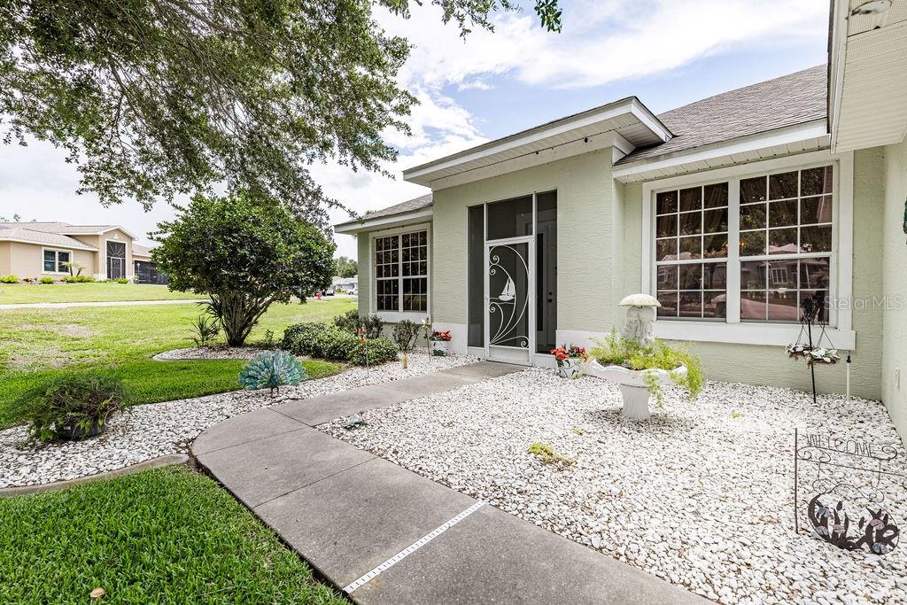 A light green house with a white-trimmed front entrance, a concrete walkway, and gravel landscaping — 3370 SAINT LUCIA COURT, TAVARES, FL