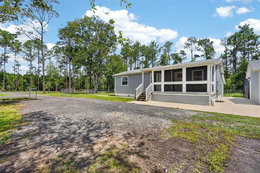 A gray house with a screened-in porch sits next to a large gravel driveway — 3798 BREEZY COURT, ORMOND BEACH, FL