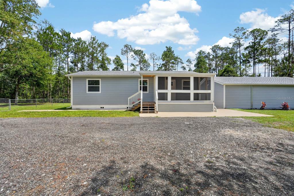A light gray house features a screened-in porch, a gravel driveway, and a detached garage — 3798 BREEZY COURT, ORMOND BEACH, FL
