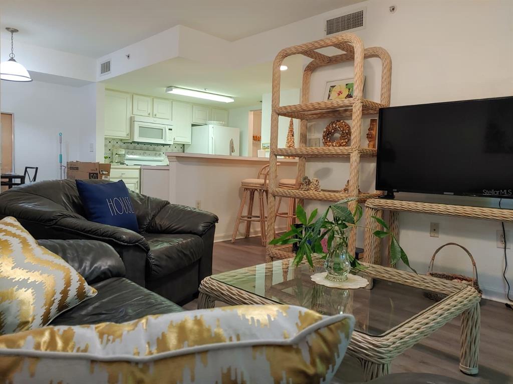 A living room features a glass-topped wicker coffee table, matching shelving, and dark leather seating — 4122 RESIDENCE DR UNIT 102, FORT MYERS, FL
