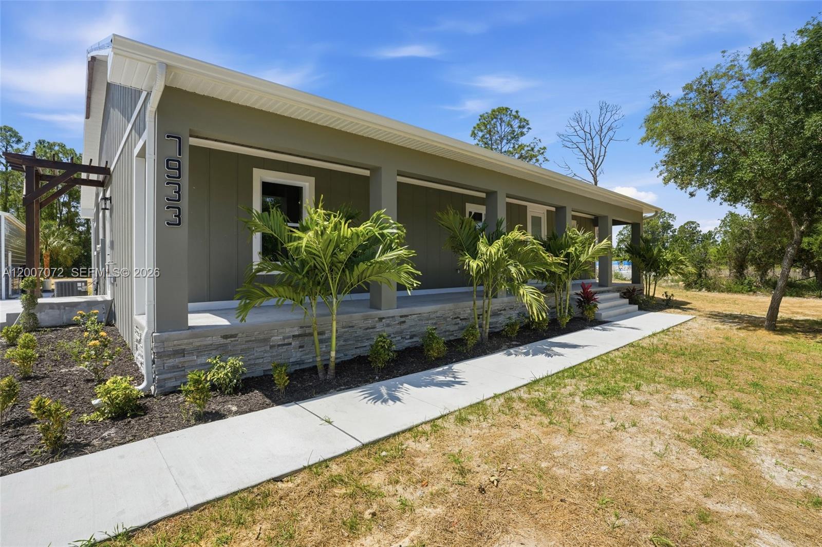 A single-story house with a covered porch, stone base, and vertical siding under a blue sky — 7933 5th TER, La Belle FL 33935, LA BELLE, FL
