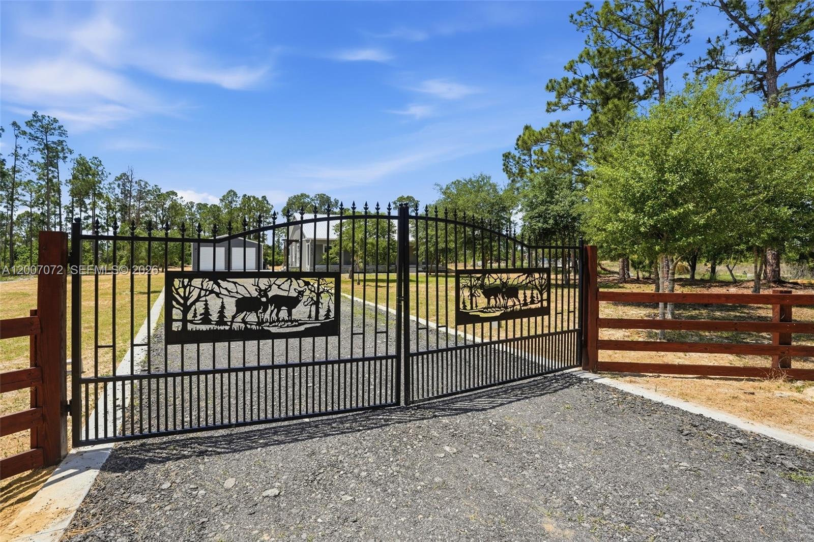 A black metal gate with deer silhouettes stands at the entrance of a gravel driveway — 7933 5th TER, La Belle FL 33935, LA BELLE, FL
