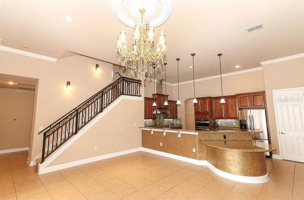 A kitchen with wood cabinets and granite countertops sits beside a staircase with iron railings — 8950 TUSCAN VALLEY PLACE, ORLANDO, FL