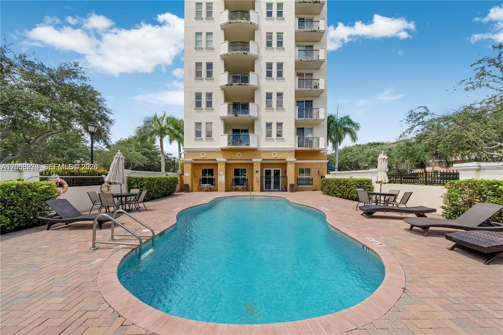 A swimming pool sits on a brick patio in front of a multi-story apartment building — 9021 SW 94th St # 509, Miami FL 33176, MIAMI, FL