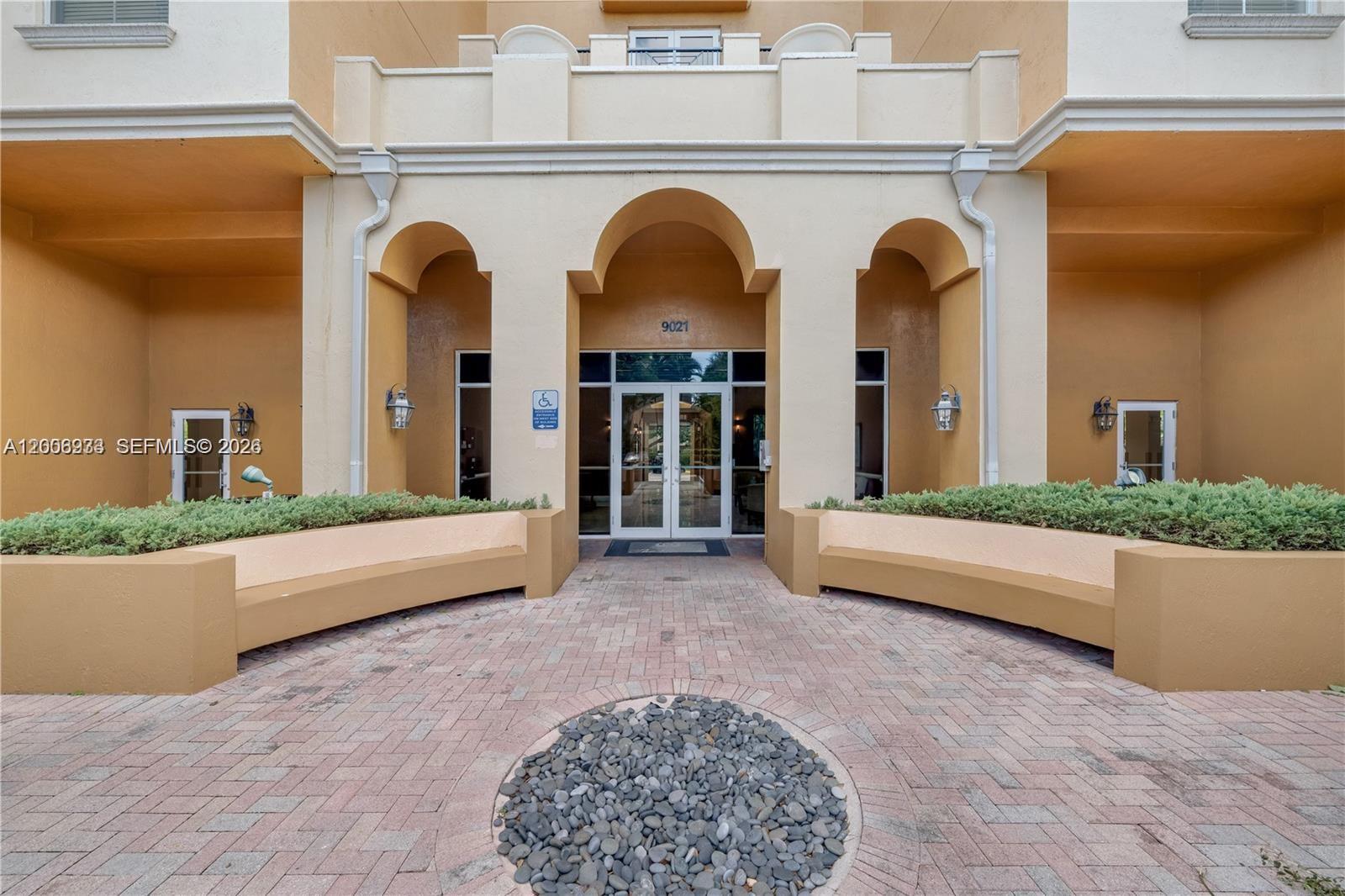 The exterior entrance of a building features arched doorways, brick paving, and built-in planters — 9021 SW 94th St # 509, Miami FL 33176, MIAMI, FL