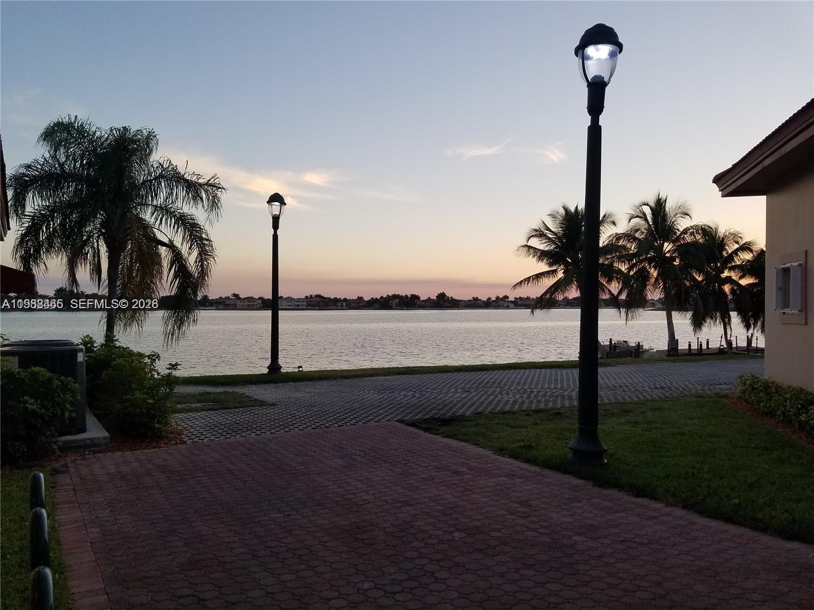A paved walkway with lamp posts overlooks a lake at sunset near palm trees — 18741 SW 25th Ct, Miramar FL 33029, MIRAMAR, FL