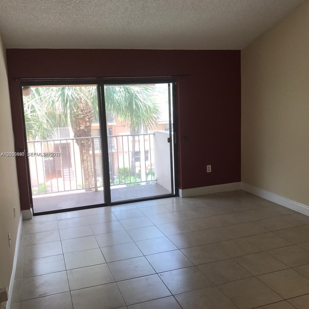 An empty room features tiled flooring, a dark red accent wall, and sliding glass balcony doors — 7200 NW 179th St # 302, Hialeah FL 33015, HIALEAH, FL