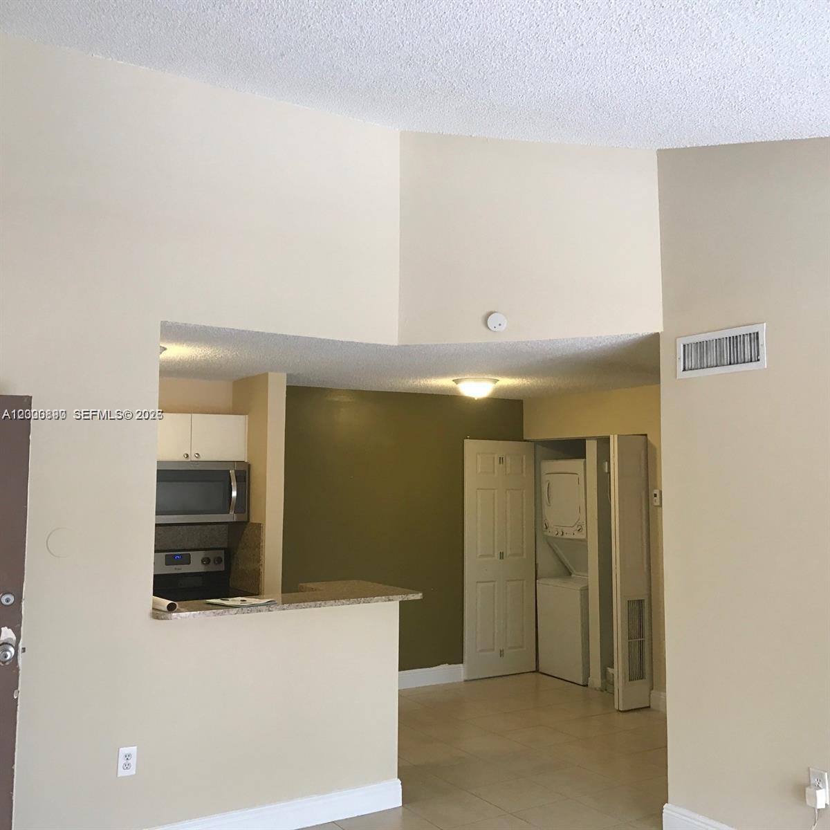 A kitchen with a breakfast bar overlooks a dining area featuring a stacked laundry unit — 7200 NW 179th St # 302, Hialeah FL 33015, HIALEAH, FL