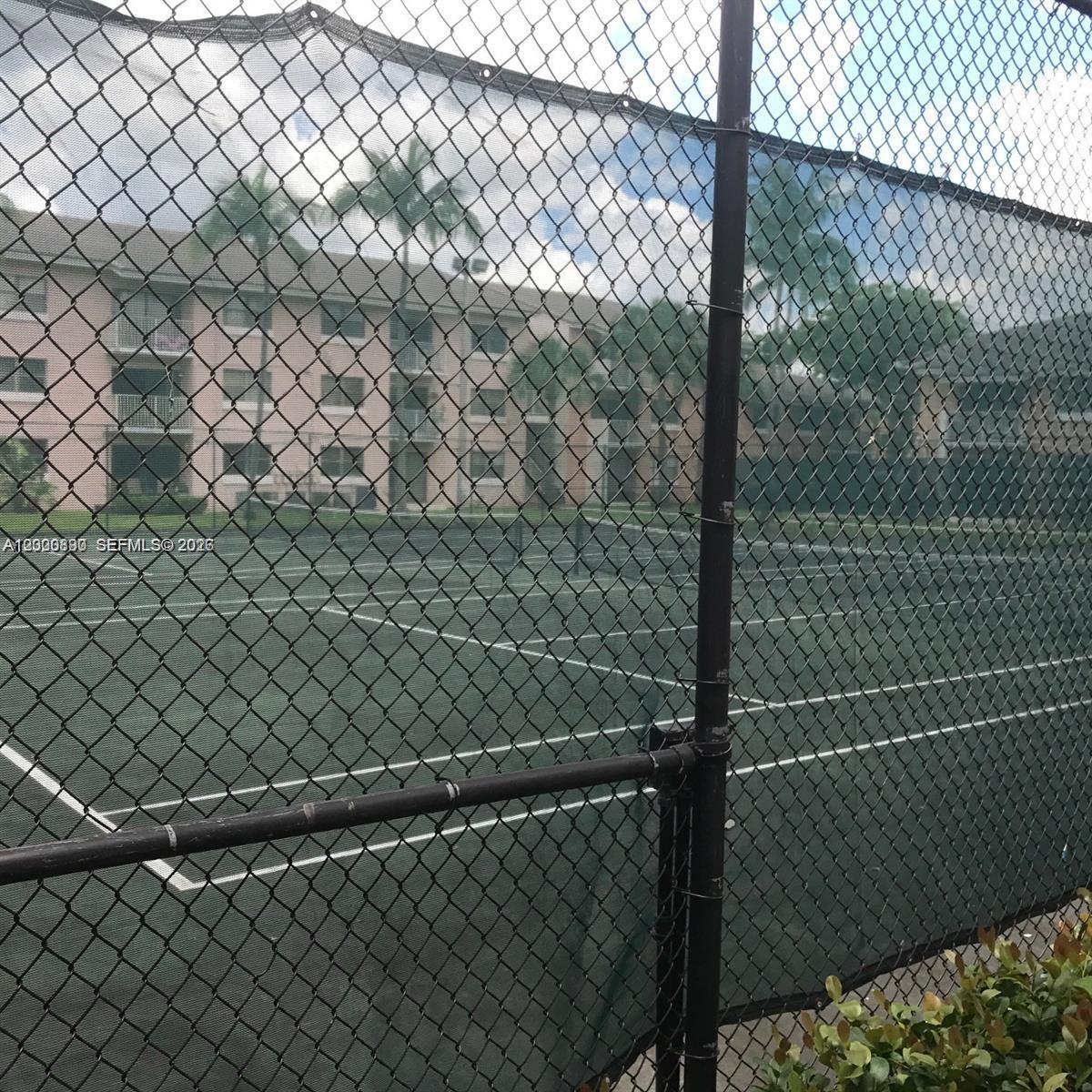 A chain-link fence encloses a tennis court in front of a multi-story apartment building — 7200 NW 179th St # 302, Hialeah FL 33015, HIALEAH, FL