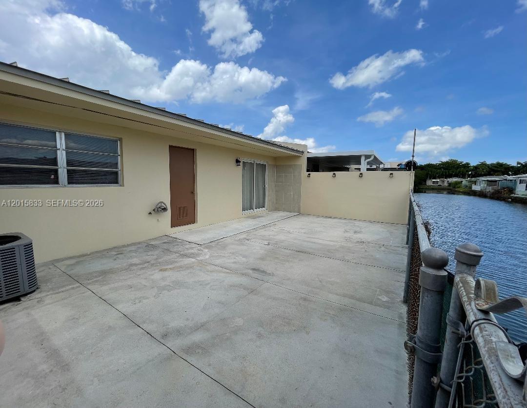 A concrete patio sits beside a house with a brown door and a canal view — 10112 SW 20th St, Miami FL 33165, MIAMI, FL