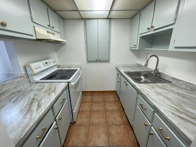 A galley kitchen features light blue cabinets, marble-patterned countertops, and brown tiled flooring — 10112 SW 20th St, Miami FL 33165, MIAMI, FL