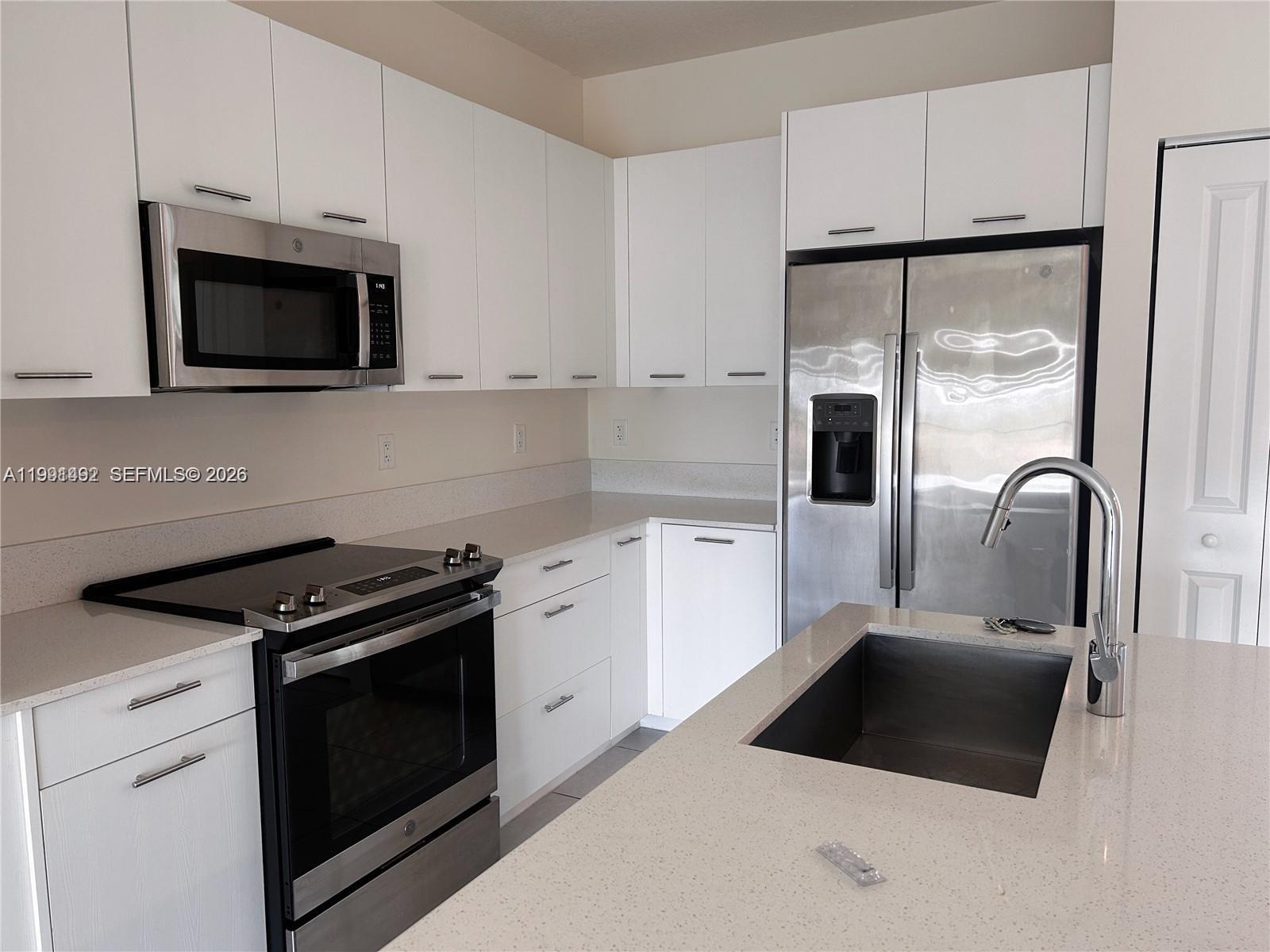 A modern kitchen features white cabinets, stainless steel appliances, and a quartz-topped island — 8001 NW 41 St # 409, Doral FL 33166, DORAL, FL