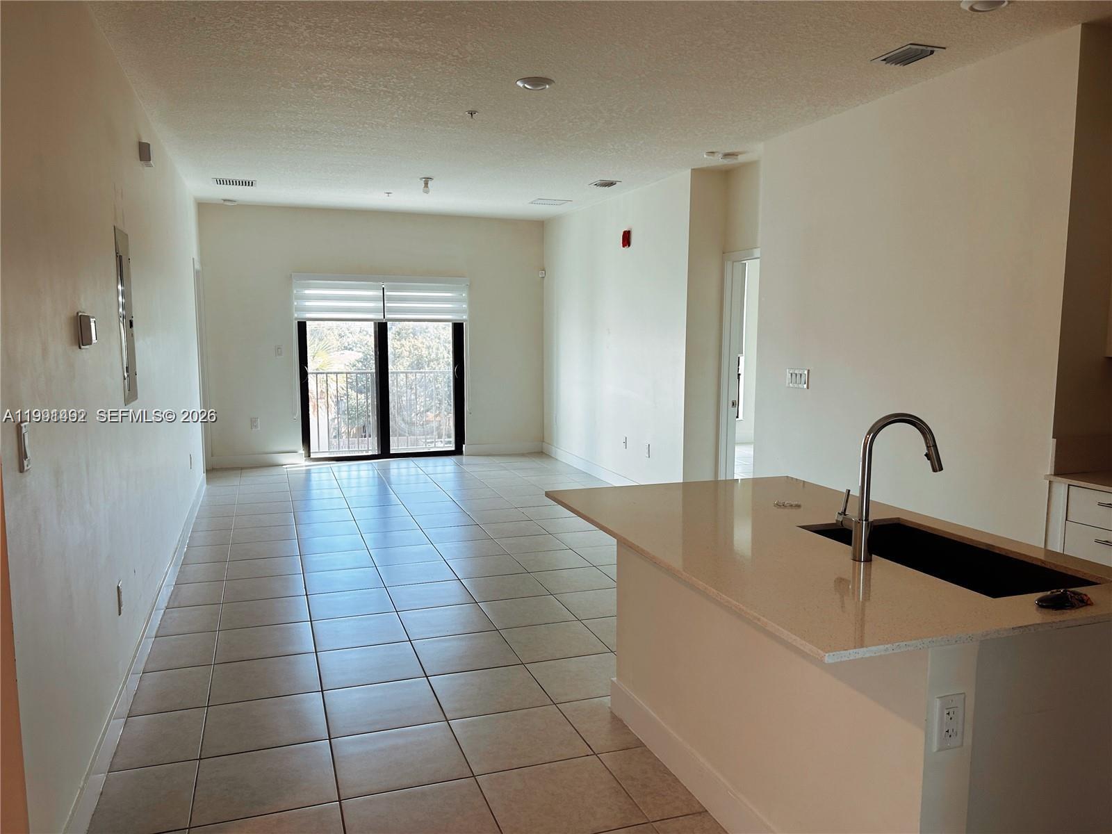An open-concept living area features light tile flooring, a kitchen island, and a sliding door — 8001 NW 41 St # 409, Doral FL 33166, DORAL, FL
