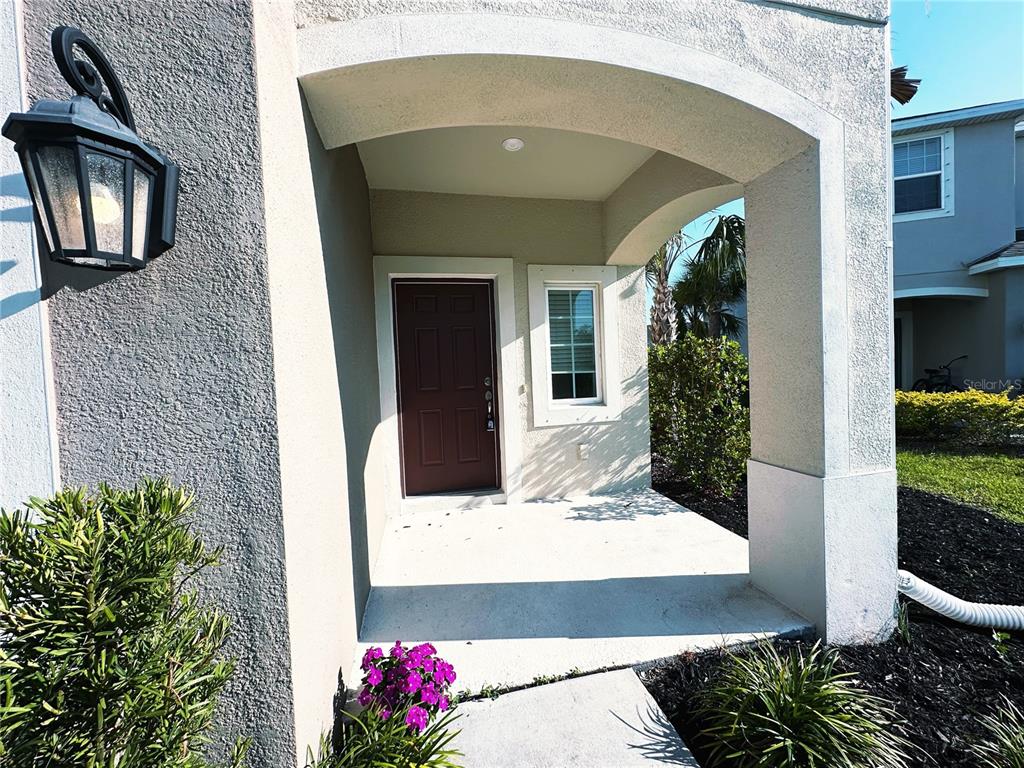 A covered entryway features a dark brown front door, a window, and a wall lantern — 5770 WINDY BAY TERRACE, NOKOMIS, FL